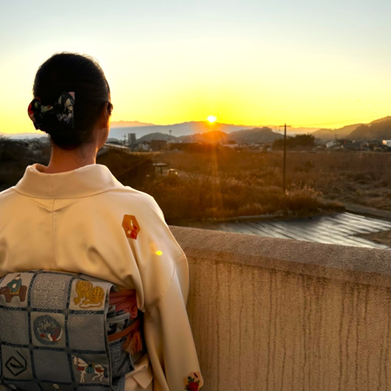 人吉温泉しらさぎ荘の女将が、着物姿で川沿いから初日の出を眺めている。