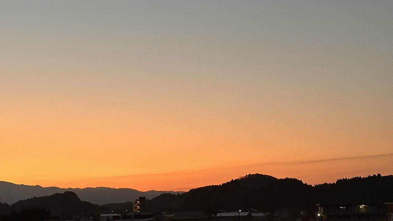 人吉温泉しらさぎ荘から望む夜明け前の空。群青から橙へと移ろう朝焼けと、山の稜線が黒く浮かび上がる静かな風景。