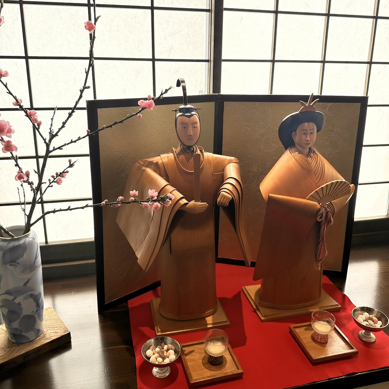 人吉球磨地方に伝わる一勝地曲げのお雛様。玄関先に飾られた木製の内裏雛と梅の花、赤い緋繊毛のしつらえ。