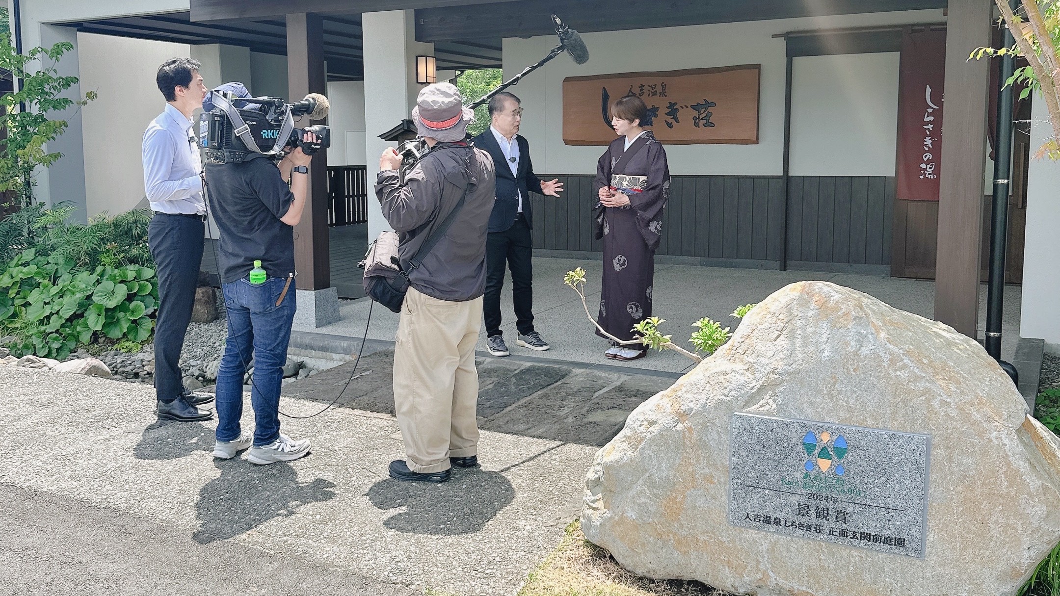RKK報道番組の取材で、人吉温泉しらさぎ荘の雨庭について説明する女将と堤伸輔さん、青谷倫太郎さん。