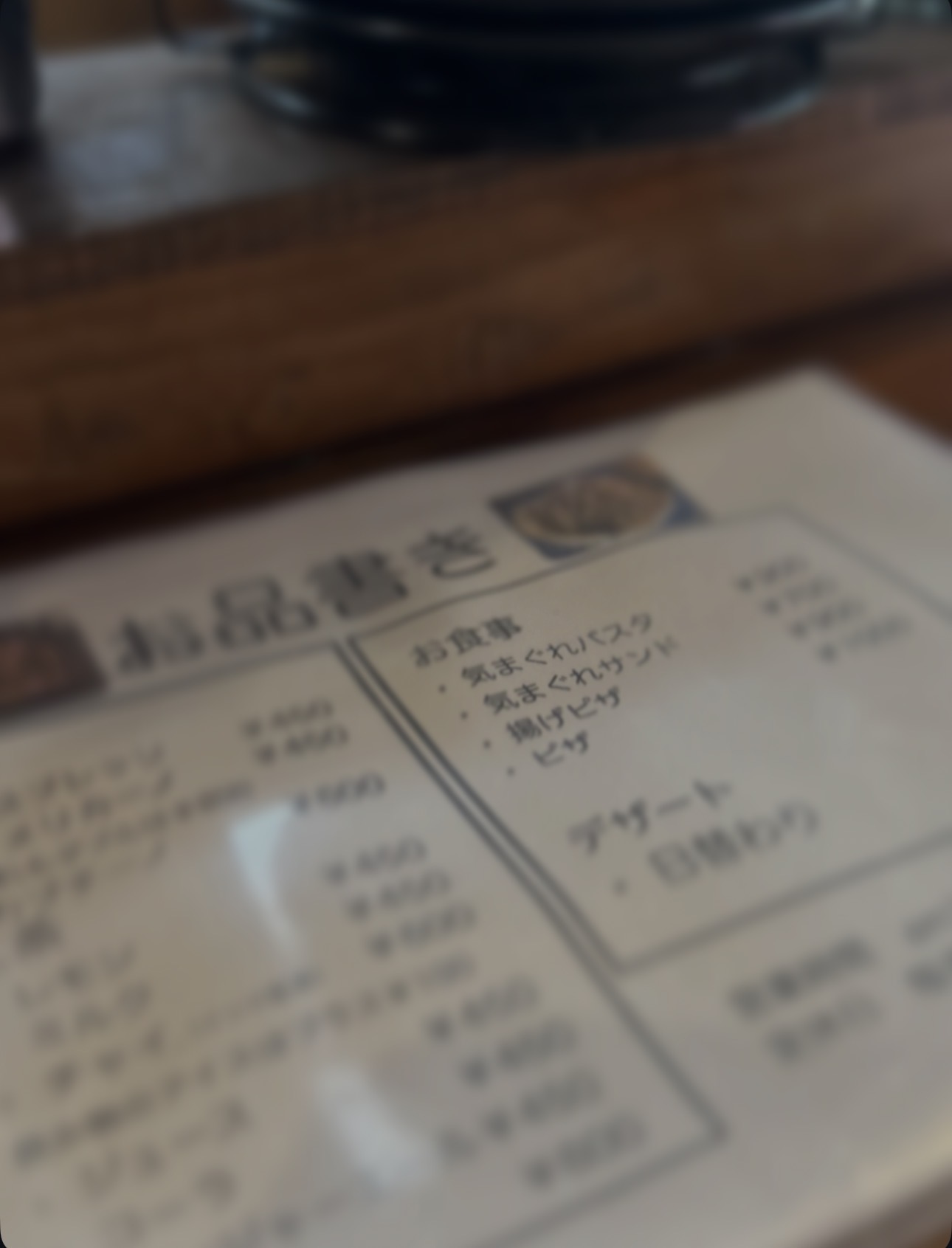 喫茶店の木製カウンターに置かれたメニュー表。気まぐれパスタなどの料理名が並び、文字が柔らかくぼけて写っている。