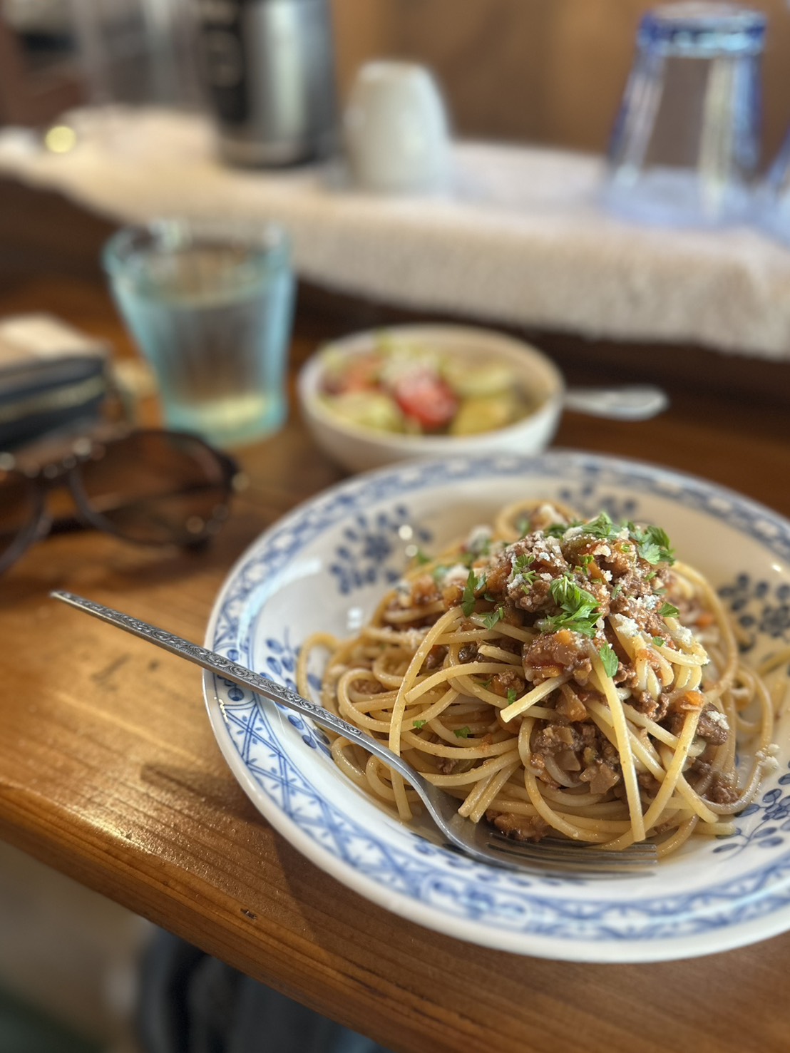 代替テキスト: 木のカウンターに置かれた青い模様の皿に盛られた気まぐれパスタ。挽き肉のソースと刻んだハーブが彩りを添えている。